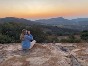 a woman sitting on a rock taking a picture of the sunset at @Nature Luxury Cottages in Nelspruit