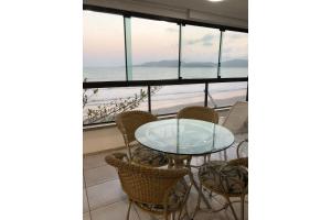 - une table en verre avec des chaises et une vue sur l'océan dans l'établissement Apartamento Frente Mar Meia Praia, à Itapema