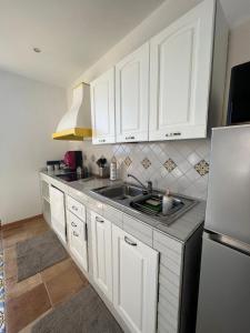 una cucina con armadi bianchi, lavandino e frigorifero di Sirenai Apartment a Colli di Fontanelle