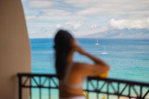 une femme assise sur un balcon donnant sur l'océan dans l'établissement Royal Lahaina Resort & Bungalows, à Lahaina