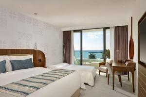 a hotel room with two beds and a desk and a window at Parklane, a Luxury Collection Resort & Spa, Limassol in Limassol