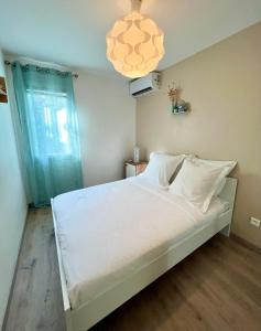 Appartement Idéal في بيتي-بور: غرفة نوم مع سرير مع شراشف بيضاء وثريا