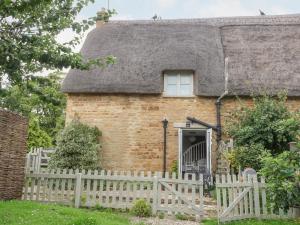 a brick house with a thatched roof with a white fence at Honeysuckle Cottage Brailes in Sutton under Brailes