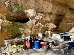 a kitchen with two tables and appliances next to a stone wall at Hatter's Hideout Cave and Lodge in Newnes Junction