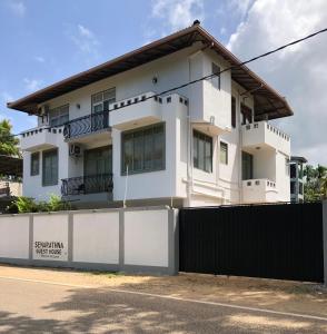a white house with a black fence at senarathna guest house in Weligama