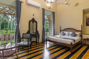 a bedroom with a bed and a chair and a mirror at Silva Heritage Resort Goa in Benaulim