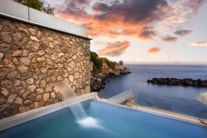 a blue swimming pool next to a stone building with the ocean at Ischia Blu Resort in Ischia