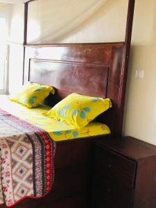 a bed with two yellow pillows and a wooden headboard at Deux-Palmes-Kribi, proche de la plage, confortable et adapté aux familles in Kribi