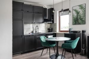 a kitchen with black cabinets and a table and green chairs at Wola Modern Apartment in Warsaw