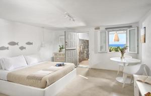 a white bedroom with a bed and a table and a window at VLIA MAR Myconian Residences in Kalafatis