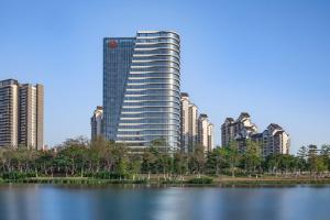a tall building next to a lake in front of a city at Sheraton Guangzhou Nansha Hotel in Guangzhou