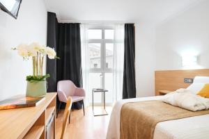 a bedroom with a bed and a desk with a vase of flowers at Hotel Don Manuel in Gijón