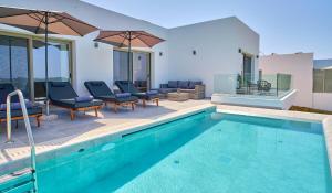 a swimming pool with chairs and umbrellas next to a house at Polgar Villas Corfu in Kavvadádes