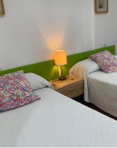 a bedroom with two beds and a lamp on a night stand at Apartamentos Alcañiz, Alicia in Alcañiz