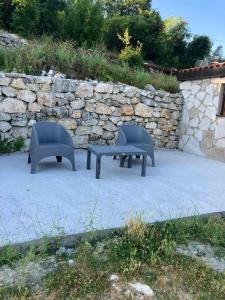 duas cadeiras e um banco em frente a uma parede de pedra em Stone house em Cetinje