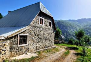 un ancien bâtiment en pierre avec un toit noir et un chemin de terre dans l'établissement Mountain Vista Guesthouse Shkafi, à Shkodër