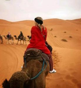 a woman riding on the back of a camel in the desert at Camp Sahara Dunes in Mhamid
