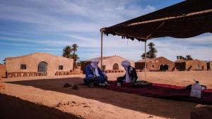 dos personas sentadas bajo un paraguas en el desierto en Camp Sahara Dunes en Mhamid