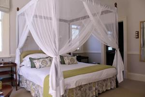 1 dormitorio con cama con dosel y cortinas blancas en Hacklewood Hill Country House, en Port Elizabeth
