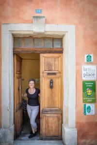 una mujer está de pie en una puerta de madera en Des Lits Sur La Place, en Hérépian