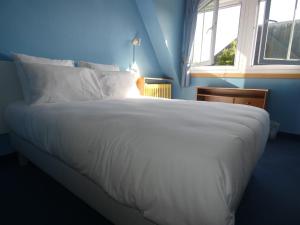 un grande letto bianco in una camera blu con finestra di Hôtel de France a Pont-lʼÉvêque