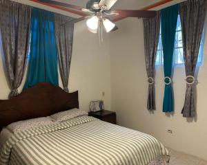 a bedroom with a bed with blue curtains and a ceiling fan at La Difference Guest House in Cap-Haïtien