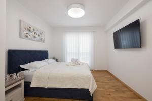 een witte slaapkamer met een bed en een televisie bij LuSi Apartman Makarska in Makarska