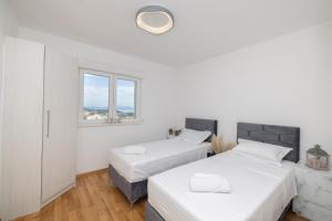 twee bedden in een witte kamer met twee ramen bij LuSi Apartman Makarska in Makarska