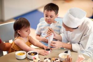 Eine Frau und zwei Kinder sitzen an einem Tisch mit Essen. in der Unterkunft Phuket Marriott Resort and Spa, Nai Yang Beach in Nai Yang Beach