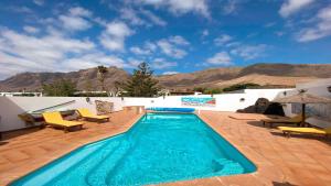 a swimming pool with a patio and mountains in the background at Bungalow Allende Famara con piscina privada y AC in Famara