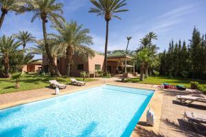 a swimming pool with palm trees and a house at Domaine Abiad in Marrakech