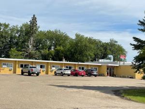 een geel gebouw met auto's geparkeerd op een parkeerplaats bij Rosthern hotel in Rosthern