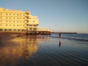 una persona parada en la playa cerca de un gran edificio en alquilaencanarias El Medano beach 1, en El Médano