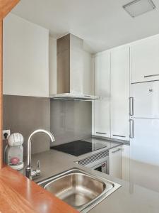 uma cozinha com um lavatório de aço inoxidável e armários brancos em Apartamento Decanelas em Sanxenxo