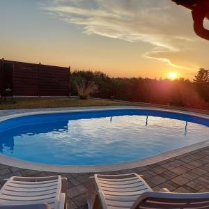 einen Pool mit zwei Stühlen und Sonnenuntergang in der Unterkunft Drvena kuca za odmor Cvetkovic brdo 