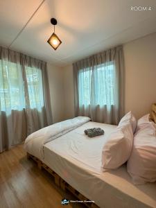 a bedroom with a bed with white sheets and windows at Qloud Cottage in Ranau
