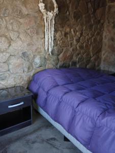 a bedroom with a purple bed and a stone wall at Cabañas Uva in Ciudad Lujan de Cuyo