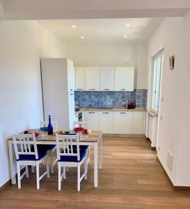 una cocina con mesa y sillas y una cocina con armarios blancos. en Due Golfi Apartment, en SantʼAgata sui Due Golfi