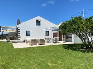 a white house with chairs and an umbrella at Casa das 7 Lombas in Povoação