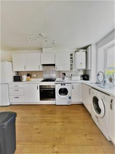 cocina con armarios blancos, lavadora y secadora en Beautiful 4 Bedroom Treasure home en Hemel Hempstead