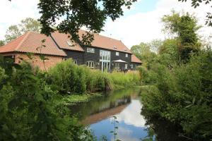 a building next to a river in front of a building at Old Oak Barn - Beautiful barn conversion with wonderful Jacuzzi hot tub in Stowmarket