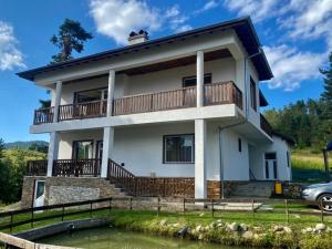 a white house with a balcony and a pond at Вила Слънчев Бряг in Dospat