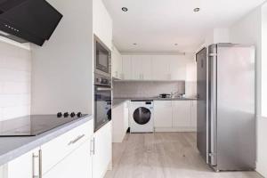 una cucina con armadi bianchi e frigorifero in acciaio inossidabile di Lovely 3 bedroom flat in North London a Londra
