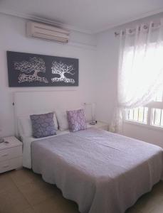 een witte slaapkamer met een groot bed met paarse kussens bij Casa JC in Orihuela