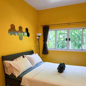 Un dormitorio con una cama con paredes amarillas y una ventana en โรงแรมบ้านเพิ่มสุข อิมแพ็ค เมืองทอง, en Pak Kret