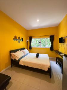 a bedroom with a bed with yellow walls and a window at โรงแรมบ้านเพิ่มสุข อิมแพ็ค เมืองทอง in Pak Kret