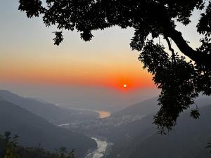 een uitzicht op een rivier met de zonsondergang op de achtergrond bij Wild Mountain Homestay in Rishīkesh