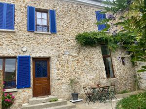 Casa de piedra con persianas azules y mesa en Chez Myriam en Orgeval
