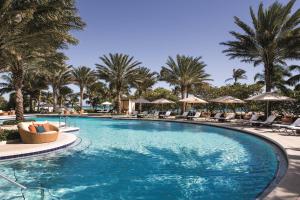 a swimming pool with chairs and palm trees at The Ritz-Carlton Bal Harbour, Miami in Miami Beach