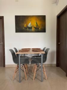 a dining room table with chairs and a painting of ships at Hermoso hogar con bbq y piscina en Punta Blanca in Punta Blanca